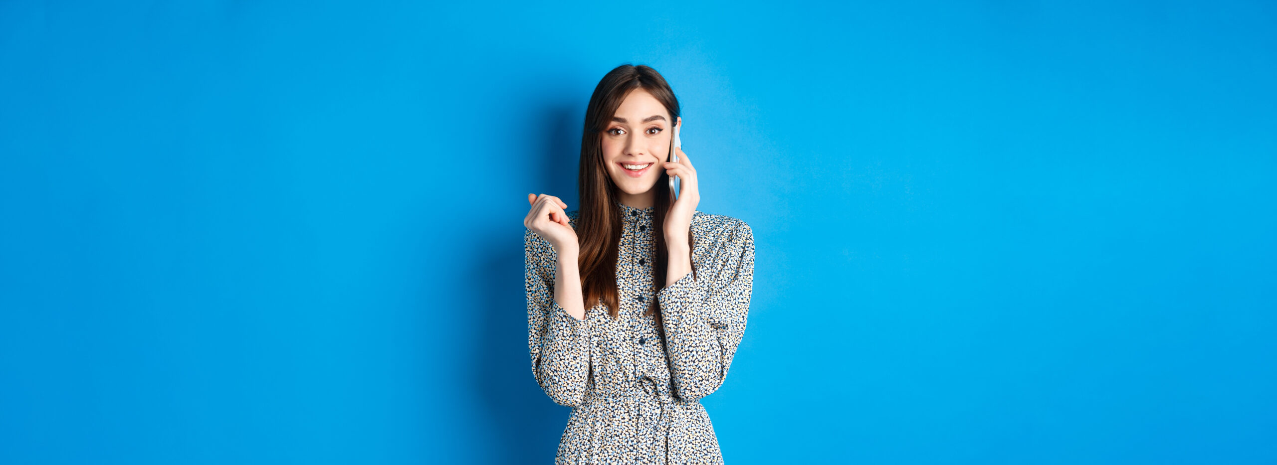 Excited woman receive good news on mobile phone, smiling happy, talking on smartphone, standing on blue background